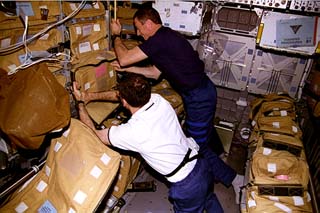 Wisoff and Baker pack soft stowage bags in their rack in the Spacehab module